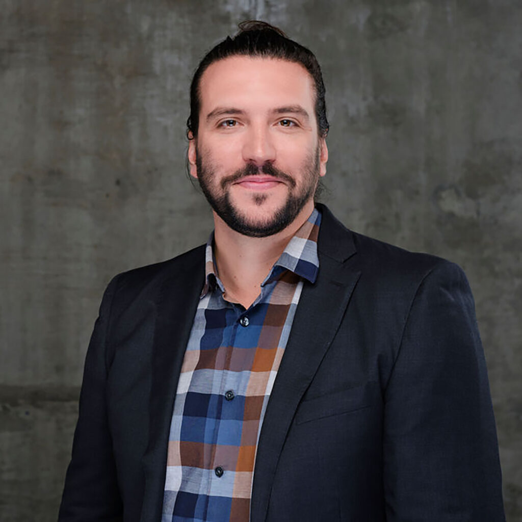 A man with a beard wearing a suit smiles at the camera.